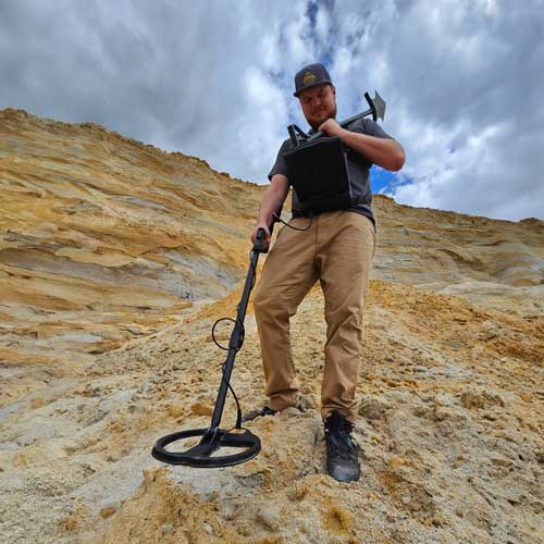 Person using a metal detector on a sandy landscape